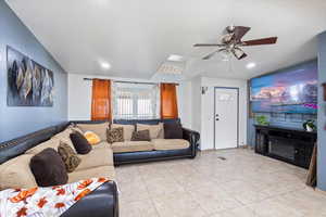 Living area with light tile patterned floors, ceiling fan, a glass covered fireplace, and recessed lighting