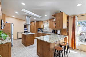 Kitchen featuring light stone countertops, a kitchen island, recessed lighting, brown cabinets, and a breakfast bar area