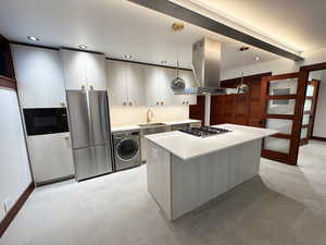 Kitchen featuring light countertops, island range hood, appliances with stainless steel finishes, decorative light fixtures, and washer / dryer