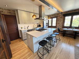 Kitchen featuring hanging light fixtures, a center island, island range hood, a breakfast bar area, and light wood-type flooring