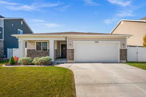 View of front of property with stone siding, concrete driveway, an attached garage, a porch, and fenced yard.
