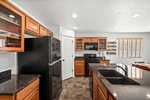 Kitchen featuring glass insert cabinets, black appliances, stone finish floors.