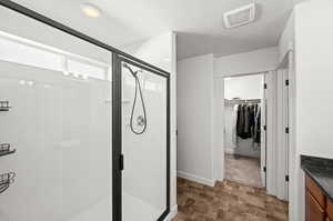 Bathroom with a walk in closet, stone finish floors, a shower stall, and vanity