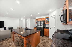 Kitchen with an island with sink, black appliances, a kitchen bar, dark stone counters, and recessed lighting