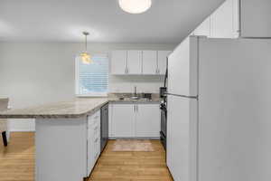 Kitchen with freestanding refrigerator, light countertops, white cabinetry, and a peninsula