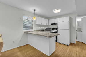 Kitchen with freestanding refrigerator, a peninsula, light countertops, range with gas cooktop, and hanging light fixtures