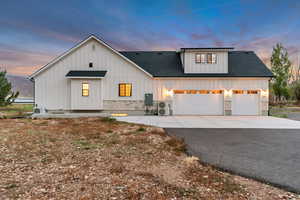 Modern farmhouse with board and batten siding, driveway, a shingled roof, and stone siding