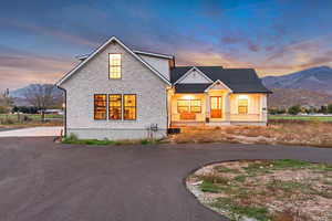 Modern farmhouse style home with a mountain view, board and batten siding, stone siding, a porch, and asphalt driveway