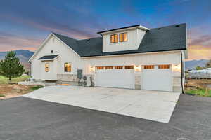 Modern inspired farmhouse with board and batten siding, roof with shingles, stone siding, driveway, and a mountain view