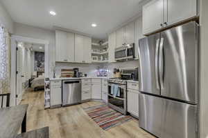 Kitchen with stainless steel appliances, open shelves, light countertops, light wood-type flooring, and white cabinets