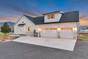 Modern inspired farmhouse featuring board and batten siding, stone siding, concrete driveway, and roof with shingles