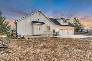 Modern farmhouse with board and batten siding, roof with shingles, driveway, and stone siding