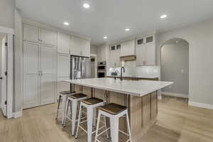 Kitchen featuring arched walkways, glass insert cabinets, light wood-style floors, recessed lighting, and stainless steel appliances