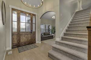 Entrance foyer featuring a chandelier, arched walkways, light wood finished floors, and stairs