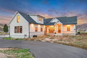 Modern inspired farmhouse with board and batten siding, stone siding, covered porch, and roof with shingles