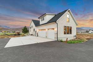 Property exterior at dusk with stone siding, a mountain view, concrete driveway, and board and batten siding