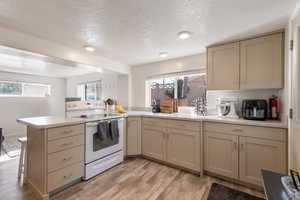 Basement Kitchen featuring cream cabinets, white electric range oven, a peninsula, light wood-style floors, and a textured ceiling