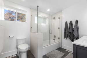 Bathroom featuring vanity, shower / bath combination with glass door, and dark tile patterned flooring