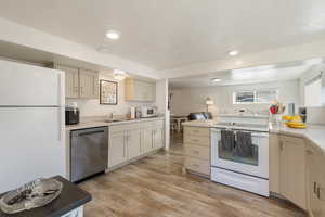 Basement Kitchen featuring white appliances, light wood-style flooring, cream cabinetry, recessed lighting, and light stone countertops