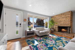 Living room featuring hardwood / wood-style floors, lofted ceiling, a stone fireplace, and recessed lighting