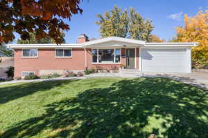 Ranch-style home featuring brick siding, a chimney, a front lawn, a garage, and concrete driveway