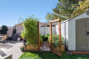 Fenced backyard featuring a storage unit, a vegetable garden, and a patio
