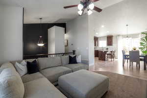 Living room featuring light wood-type flooring, a ceiling fan, a chandelier, and lofted ceiling