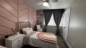 Bedroom with dark colored carpet, a textured ceiling, ceiling fan, and an accent wall