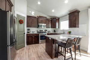 Kitchen featuring vaulted ceiling, appliances with stainless steel finishes, light stone countertops, light wood-style flooring, and a peninsula