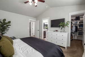 Main bedroom with a walk in closet, en-suite bath, vaulted ceiling, carpet flooring, and ceiling fan