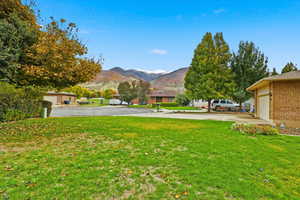View of grassy yard with a mountain view, driveway, and a garage