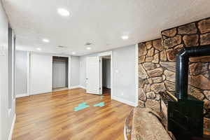 Unfurnished living room featuring a wood stove, a textured ceiling, light wood-style floors, and recessed lighting