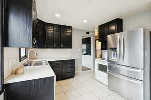 Kitchen with stainless steel refrigerator with ice dispenser, dark cabinetry, white electric stove, light countertops, and light tile patterned flooring
