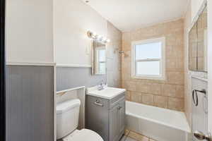 Bathroom with vanity, washtub / shower combination, light tile patterned floors, and wainscoting