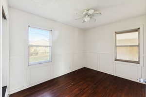 Spare room featuring a decorative wall, wainscoting, dark wood-style flooring, and a ceiling fan