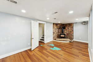 Basement with a wood stove, light wood-style flooring, stairway, recessed lighting, and a textured ceiling