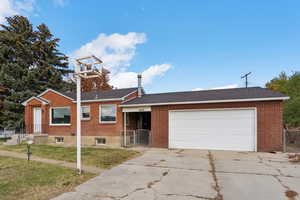 Ranch-style house with concrete driveway, brick siding, an attached garage, and a gate