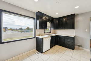 Kitchen featuring dark cabinets, light countertops, white dishwasher, light tile patterned flooring, and recessed lighting