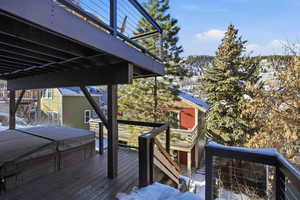 Snow covered deck featuring a hot tub, stairs, and a balcony