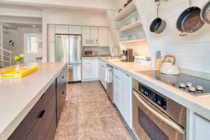 Kitchen featuring open shelves, stainless steel appliances, light stone countertops, white cabinetry, and dark brown cabinetry