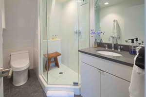 Bathroom with vanity, a shower stall, tile walls, and dark tile patterned floors