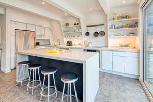 Kitchen featuring white cabinetry, a breakfast bar, open shelves, beamed ceiling, and freestanding refrigerator