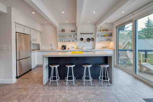Kitchen featuring open shelves, freestanding refrigerator, a kitchen breakfast bar, light stone countertops, and beam ceiling