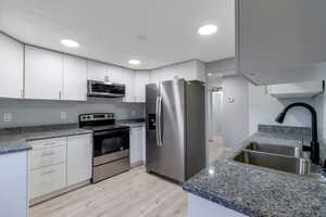 Kitchen featuring appliances with stainless steel finishes, light wood-type flooring, white cabinetry, recessed lighting, and dark stone countertops