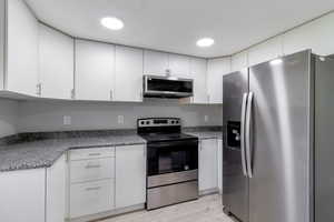 Kitchen with stainless steel appliances, white cabinetry, light stone countertops, and light wood finished floors