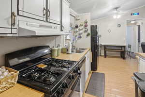 Kitchen featuring black appliances, light countertops, vaulted ceiling, light wood finished floors, and under cabinet range hood