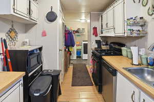 Kitchen featuring white cabinetry, black range with gas cooktop, light countertops, light wood finished floors, and dishwasher