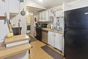 Kitchen featuring black appliances, light countertops, white cabinets, light wood-style floors, and lofted ceiling