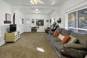 Living room featuring carpet, ceiling fan, arched walkways, and ornamental molding