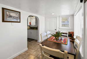 Dining space with arched walkways, light tile patterned floors, and a textured ceiling